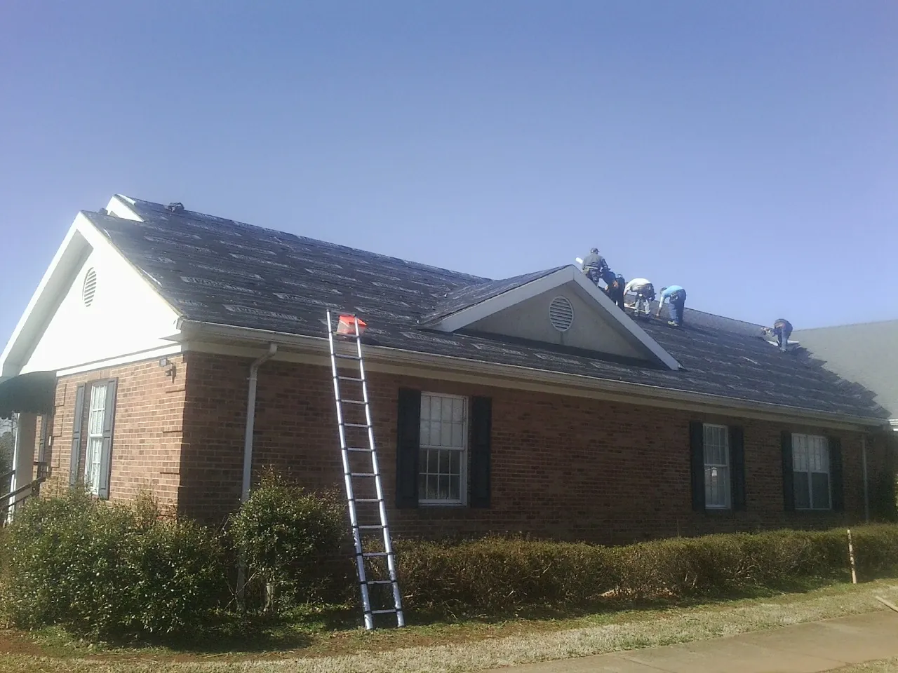 Crew tearing shingles off a brick ranch roof with a ladder set — Emergency Roof Repair work by our crew in Cape Coral