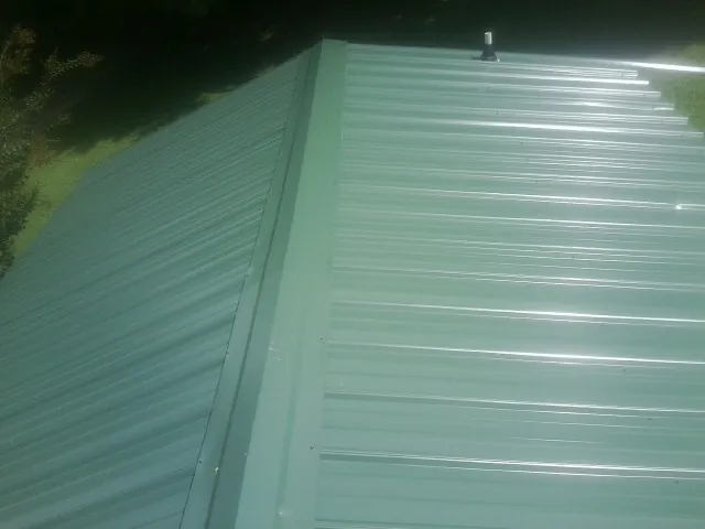 New green metal panels meeting at the ridge of a roof — Flat Roof Repair work by our crew in Cape Coral
