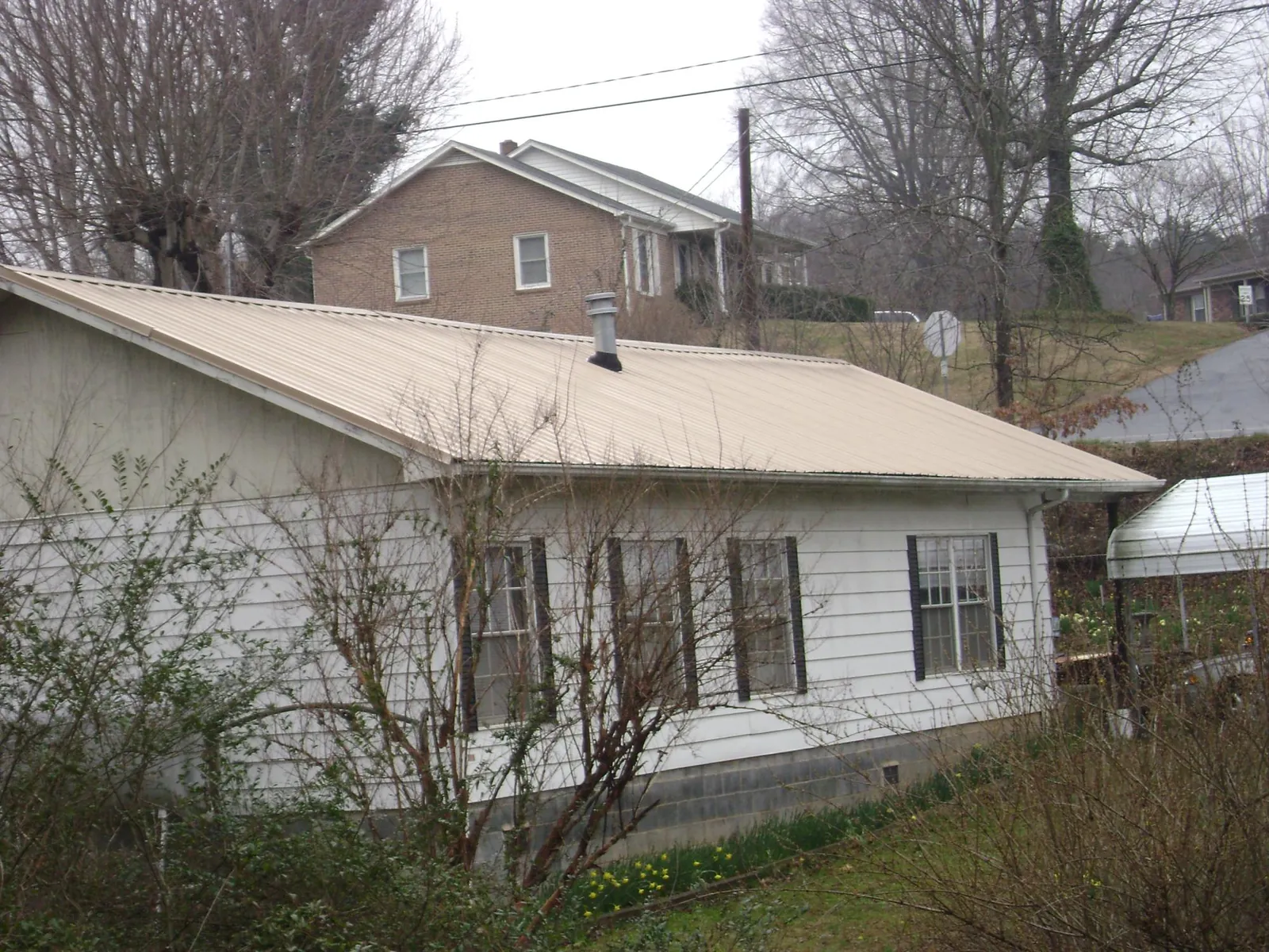 Tan metal roof on a white sided house set into a hillside — Commercial Roofing by Roofing Brothers in Cape Coral